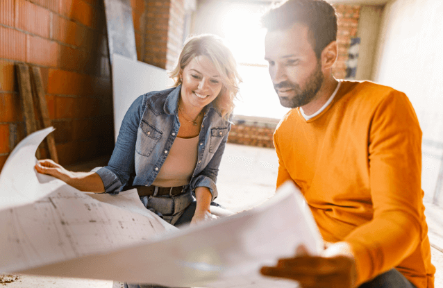 Joven pareja feliz examinando planos durante la renovación de una casa.