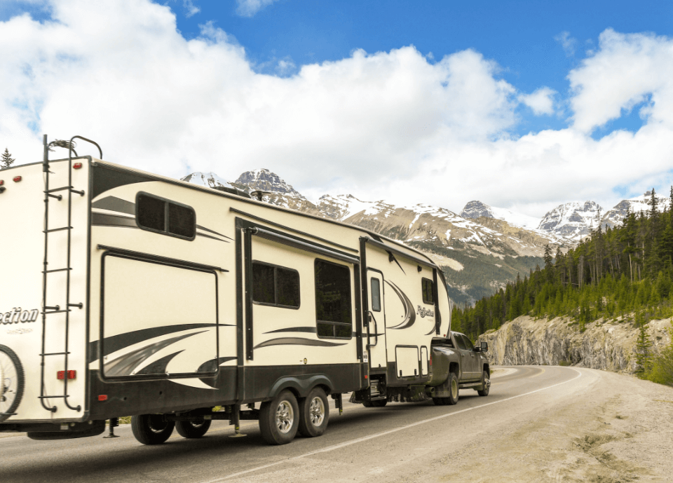 Pickup truck towing a big camping trailer on a road through the mountains.