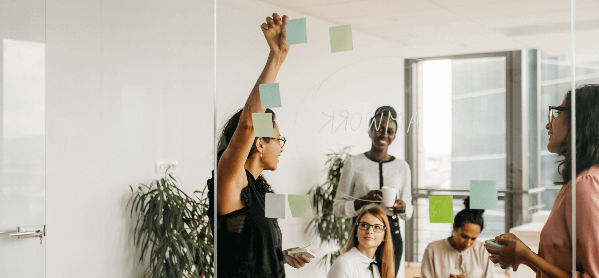 Colleagues brainstorming with adhesive notes on glass wall in office.