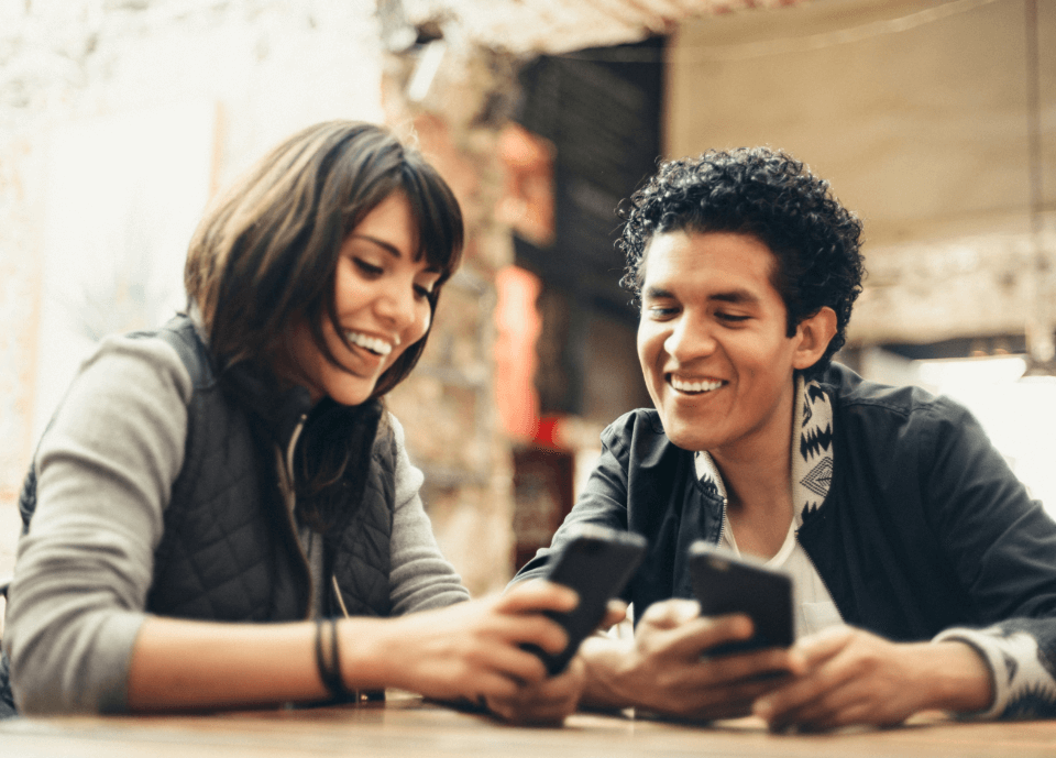 Pareja en una cafetería mirando sus teléfonos juntos.