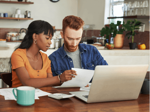 Pareja mirando documentos y sentada con su computadora portátil.