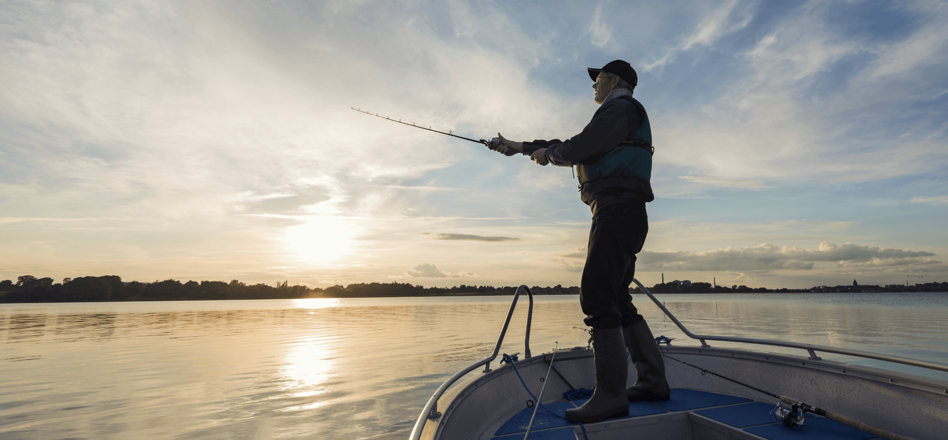 Fisherman casting out his fishing line from his boat into a flat, calm sea.