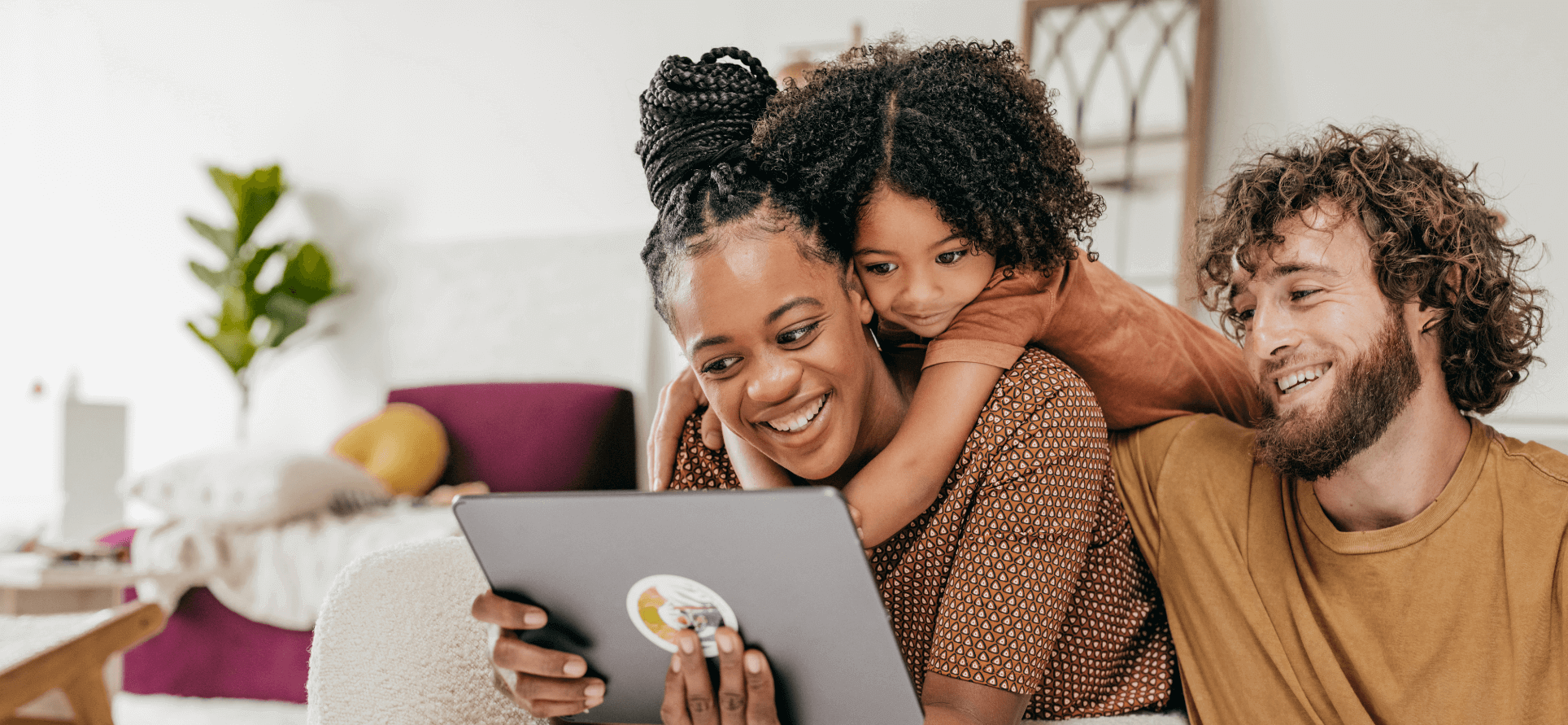 Smiling parents and daughter at home looking at a tablet.