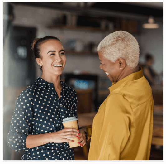 Two colleagues laughing while standing in a cafe at their workplace.