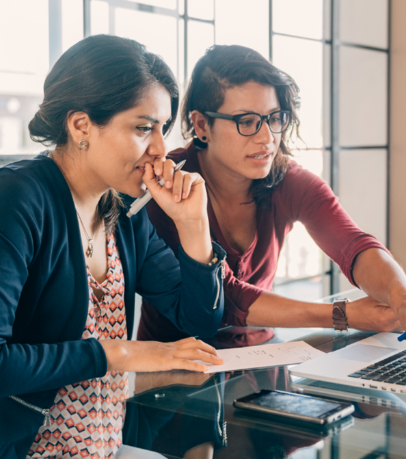 Dos compañeras sentadas frente a una computadora y trabajando juntas.
