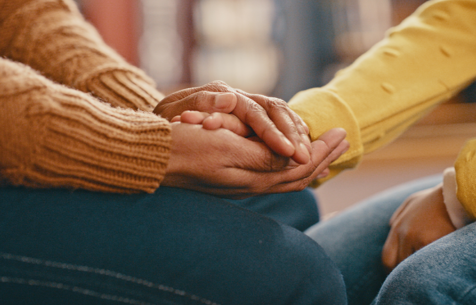 A close up of two pairs of hands, with one person clasping the other person's hands.
