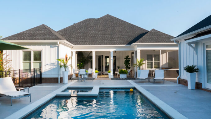 A white home with an inground pool and a wraparound patio.