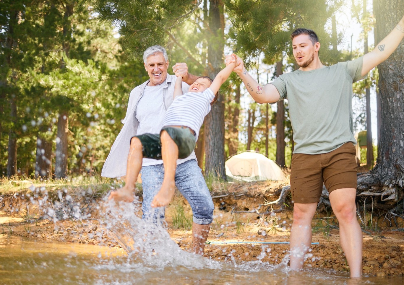 A Father and Grandfather swing a young boy playfully while standing in a lake.