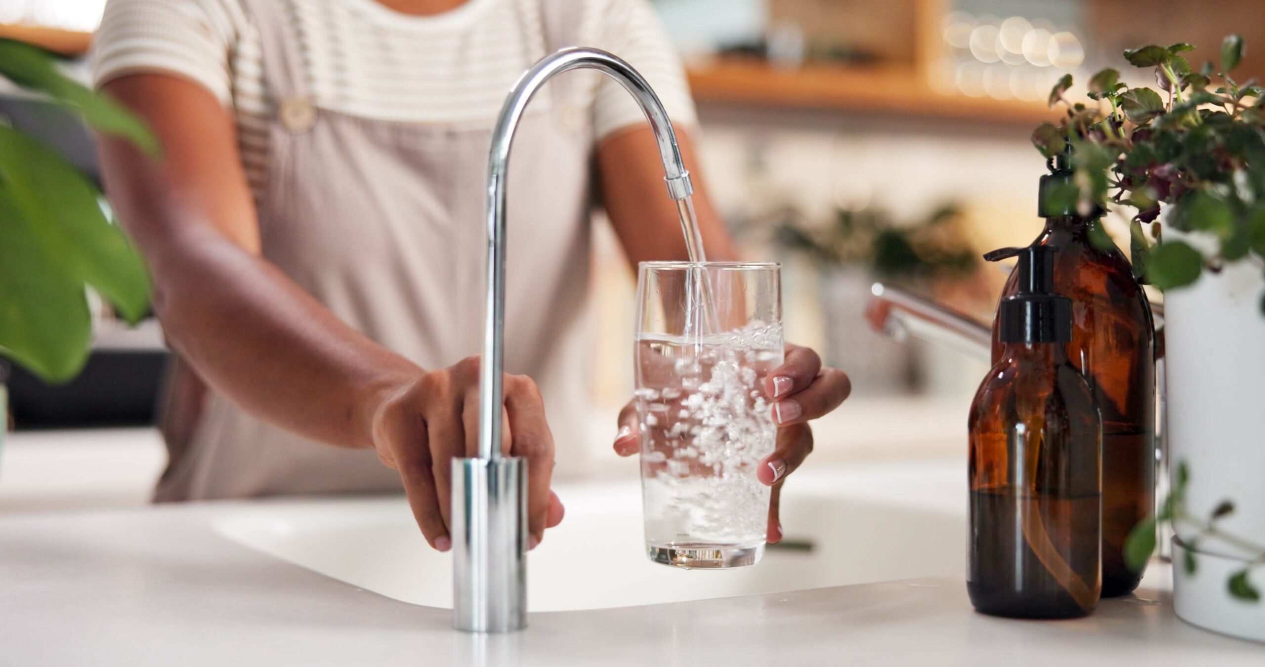 Hands, glass and water by faucet in kitchen for hydration, thirst or wellness in morning at apartment. Person, container and pouring liquid by sink with tap for drink, detox and gut health in house.