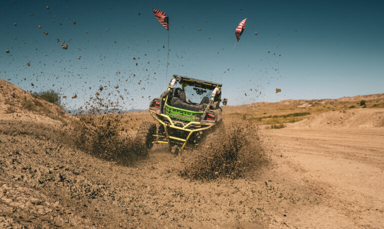 UTV Driving Away on Dirt Trail with American Flags and Flying Dust