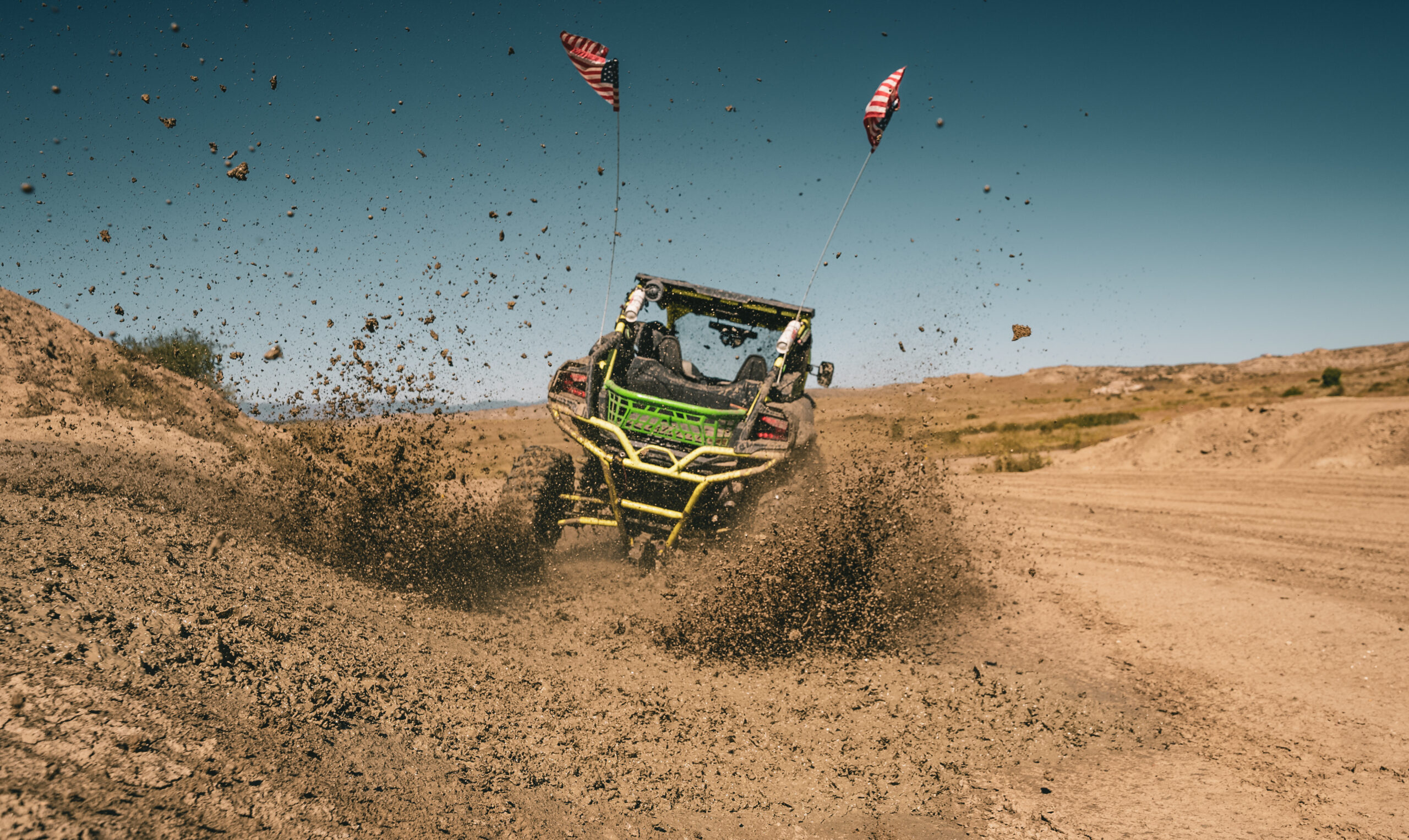 UTV Driving Away on Dirt Trail with American Flags and Flying Dust