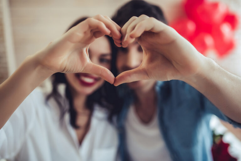 couple at home is making heart sign with hands, smiling and looking at camera.