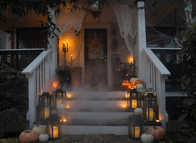A front porch is decorated for the Halloween season with spooky fog, lanterns, pumpkins and cobwebs.
