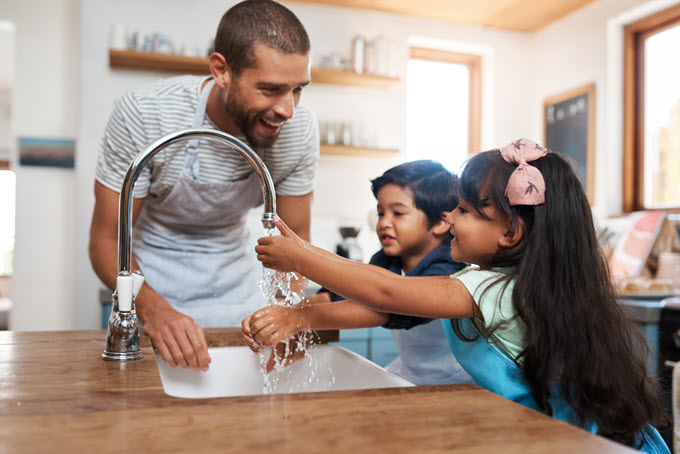 A father helps his kids wash their hands in the sink.