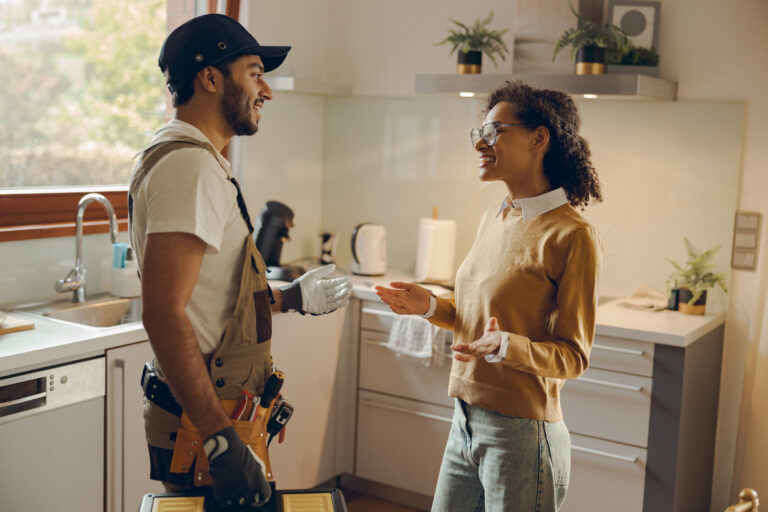 Beautiful young woman talking to male handyman while standing at the kitchen at home